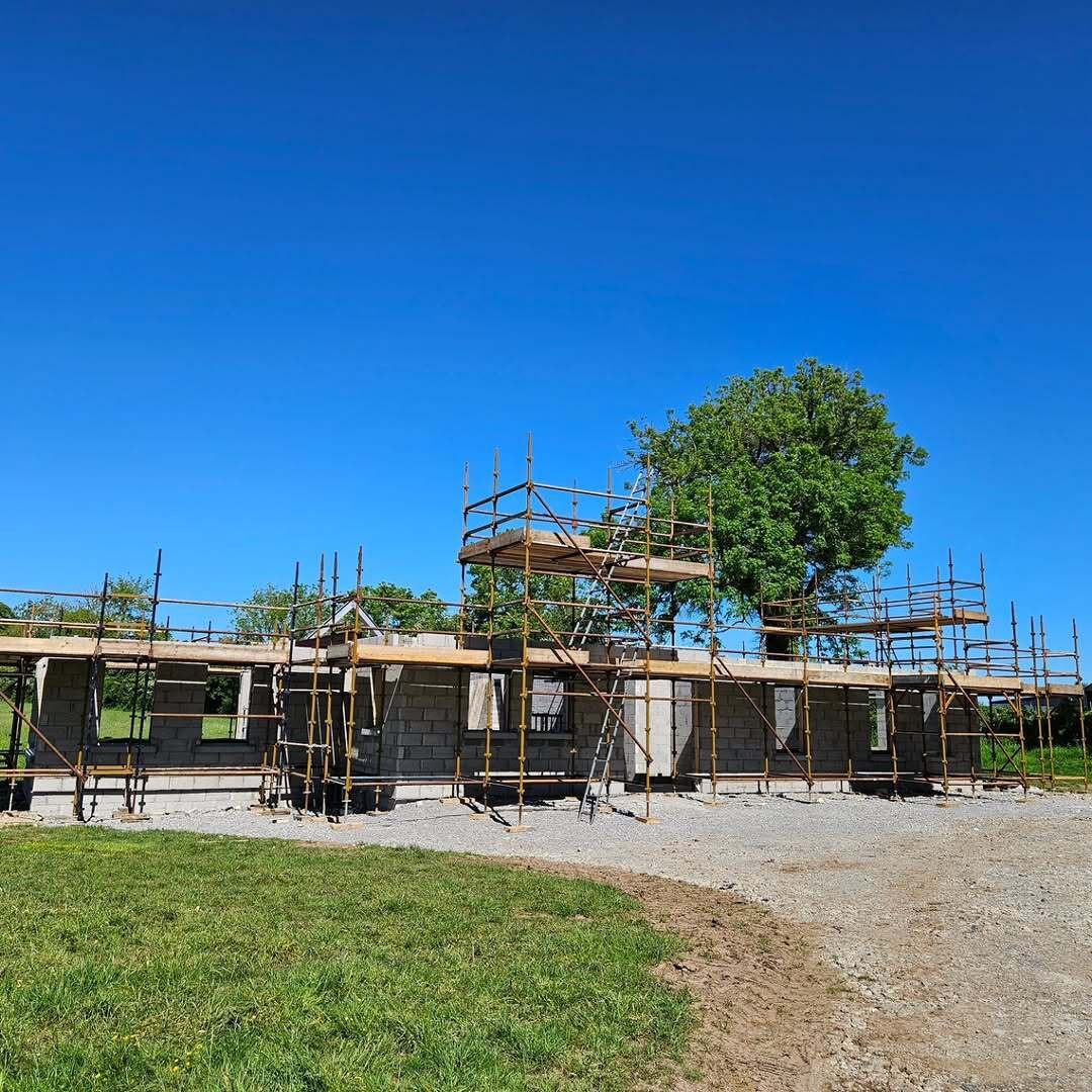 Single-storey blockwork dormer house in Kiltale wrapped in multi-level scaffolding under a clear sky