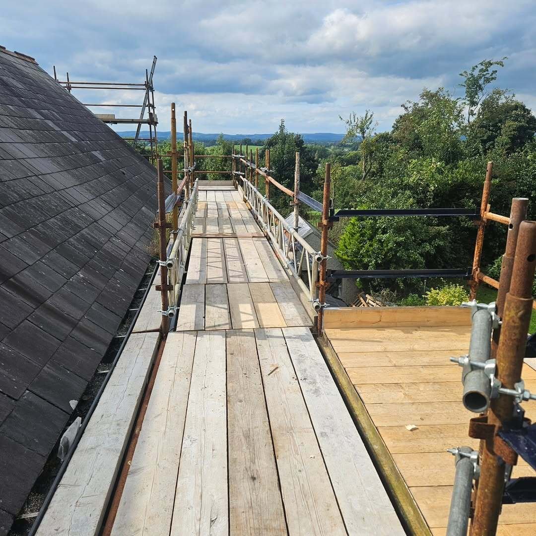 Scaffold platform running beside a slate roof with countryside views beyond