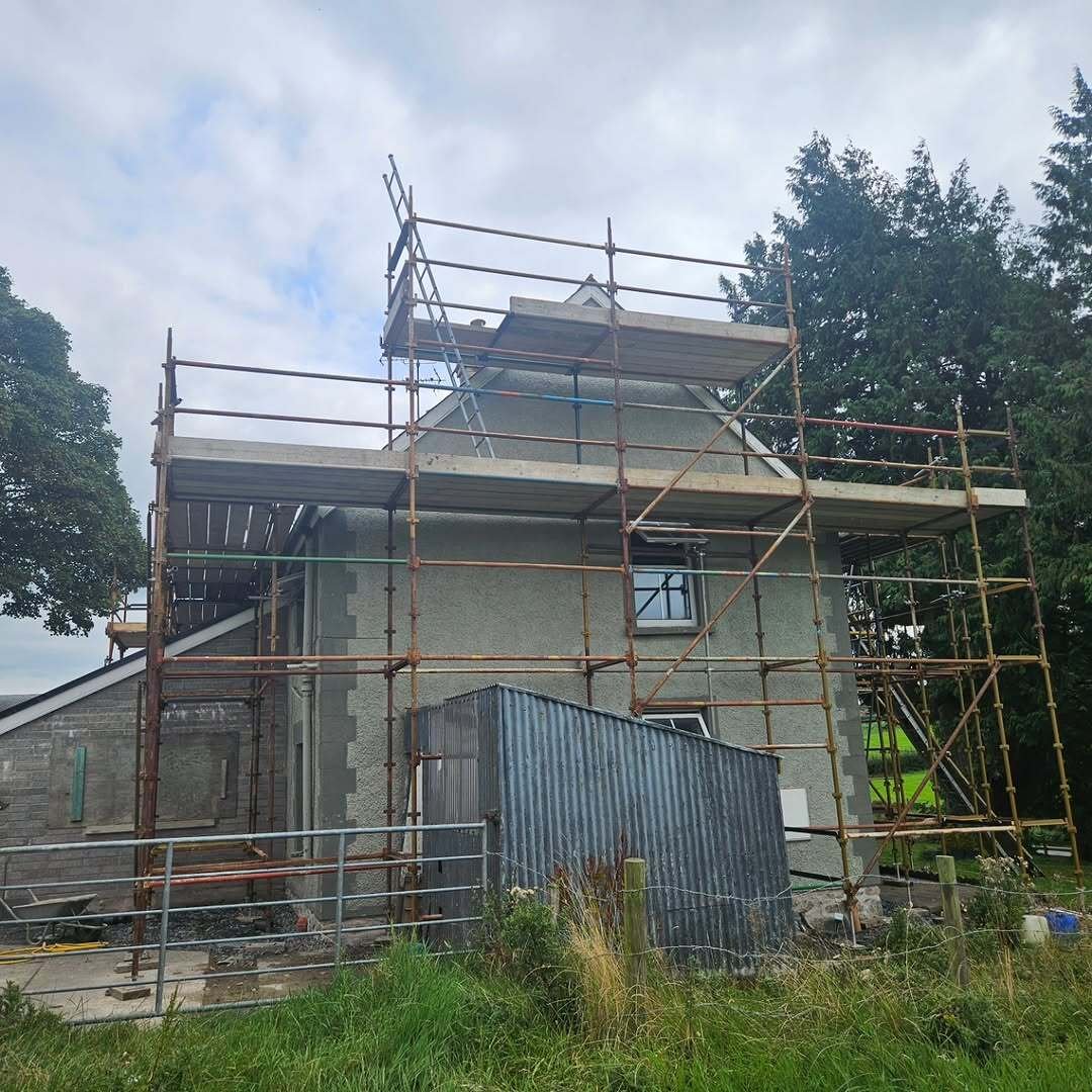 Front and side scaffold wrap on a two-storey grey house with outbuildings nearby
