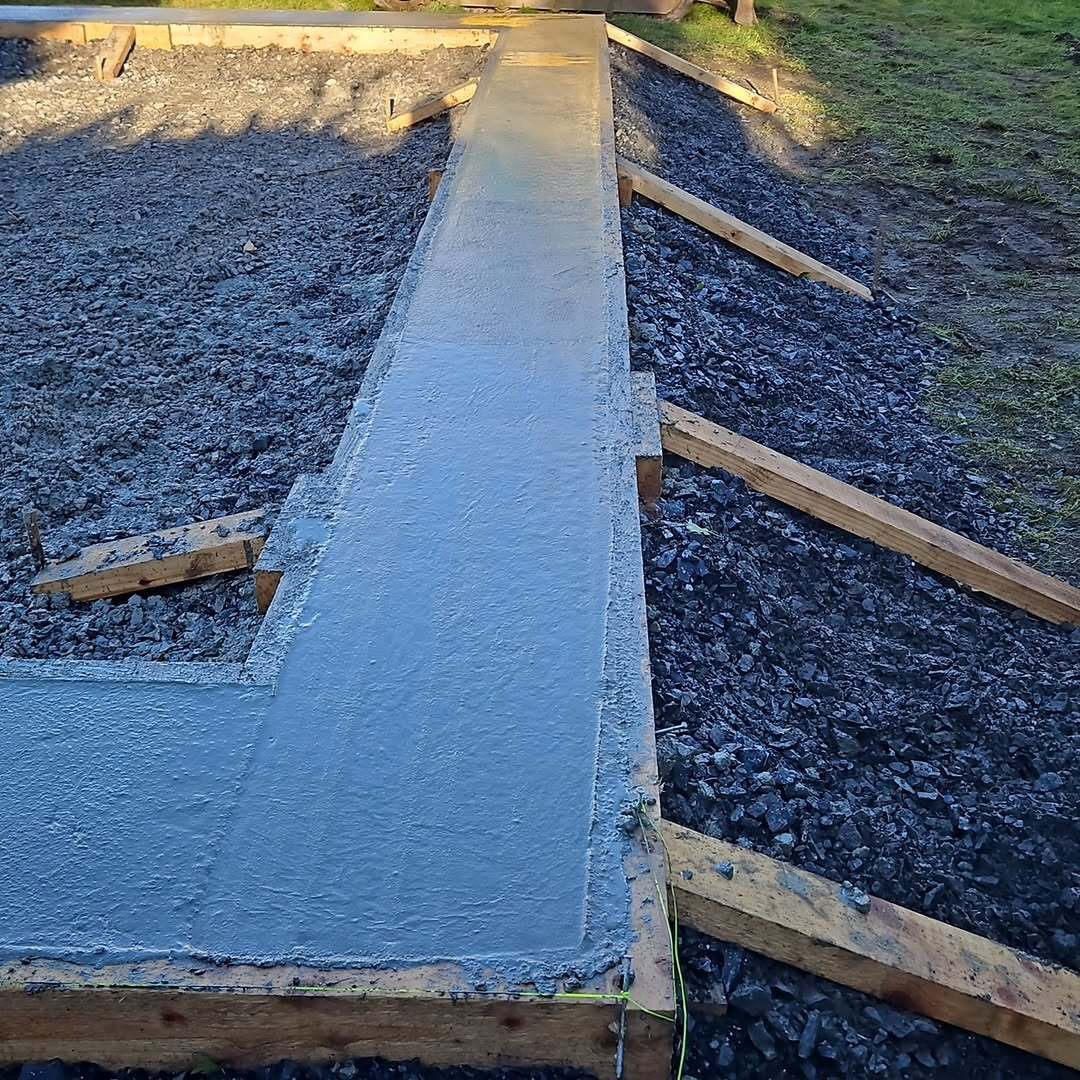 Freshly poured concrete footing levelled within timber formwork on a stone base